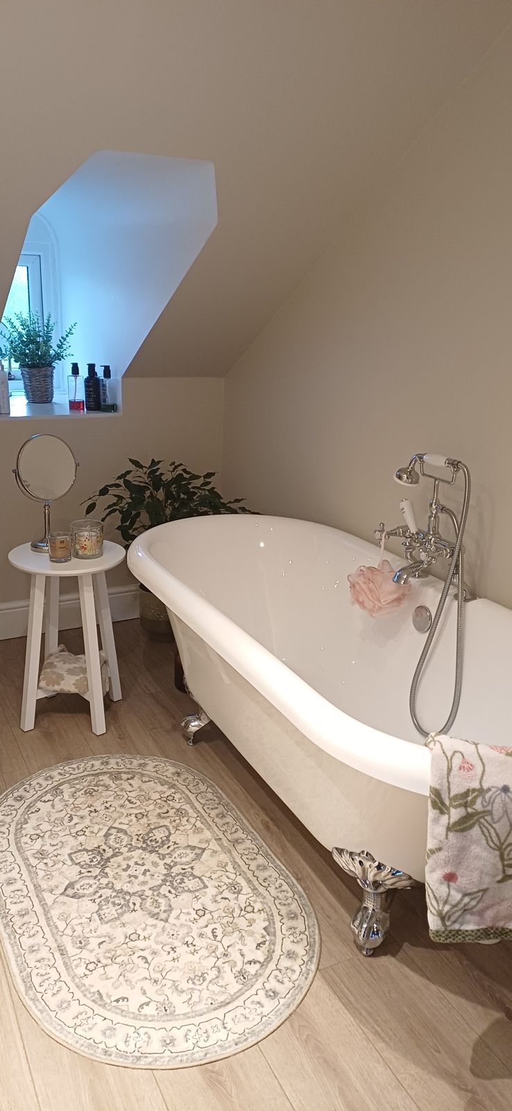 A freestanding roll-top bath under a sloping ceiling with a wood-effect floor
