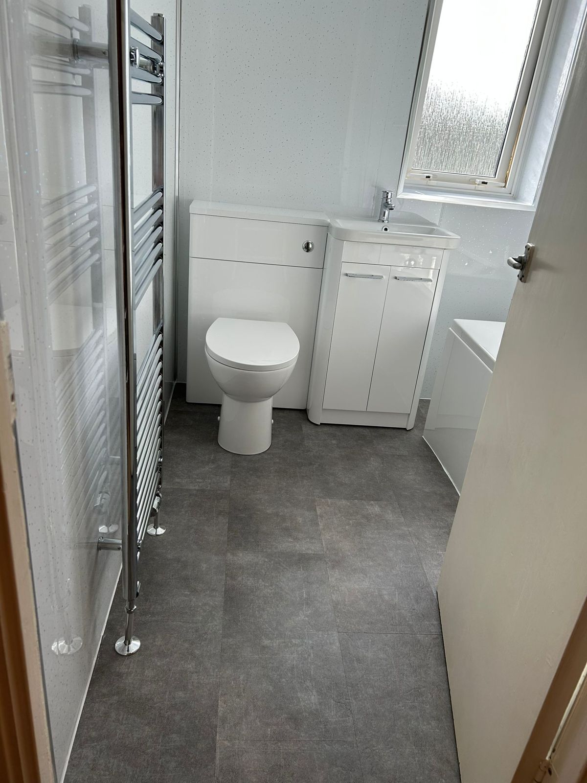 A white toilet unit and vanity beside a tall chrome towel radiator