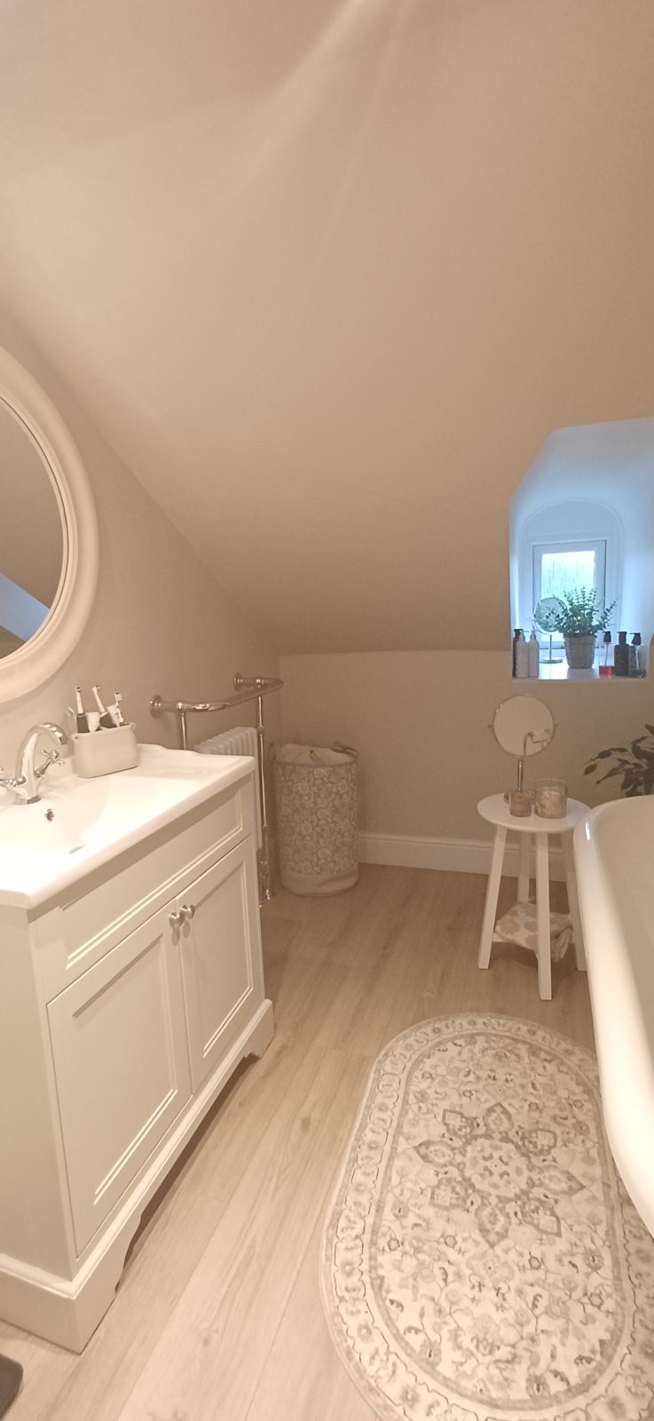 A white vanity unit and round mirror in a bright loft bathroom